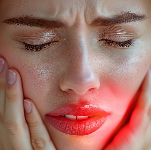 Woman with red hair closing her eyes and holding her inflamed face with both hands